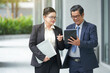 © DragonImages - Serious senior business partners walking along the street and discussing contract on tablet computer