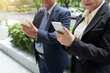 © DragonImages - Smiling business partners standing on the street and reading articles or text messages on smartphones