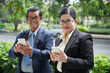 © DragonImages - Portrait of smiling senior entrepreneurs using mobile applications on smartpones and looking at camera when standing outdoors