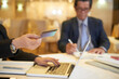 © DragonImages - Businesswoman making online order via laptop and paying with credit card when her colleague signing documents in background