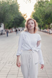 Fototapeta Konie - Portrait of a beautiful young woman in white clothes on the alley of the city