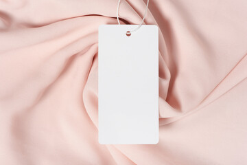 White clothing tag, label blank mockup template with the ribbon, to place your design. On a premium cotton pink fabric textile background