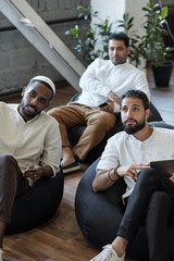 Sticker - Three young Muslim businessmen sitting in armchairs and listening to speaker or coach