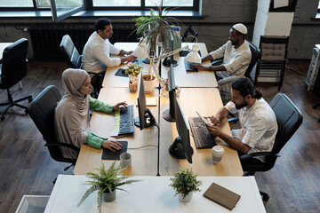 Wall Mural - Four young co-workers sitting by tables in front of computers during online work