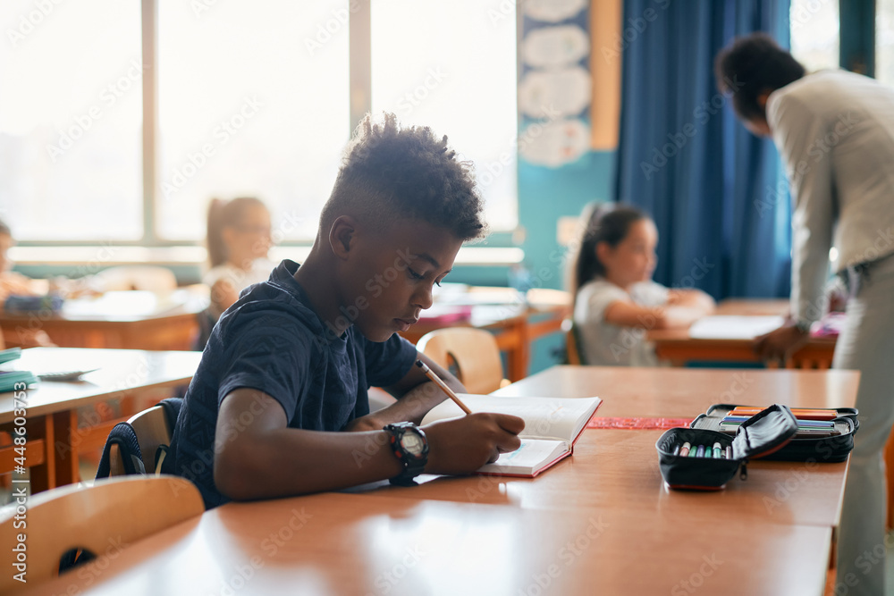 African American schoolboy writing in notebook during class at school ...
