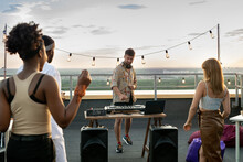 Intercultural friends dancing in front of deejay at rooftop party