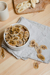 Wall Mural - Organic dried banana. Homemade dehydrated banana chips in a bowl-a healthy eating concept. Fresh banana is sliced on a board. in the kitchen on a wooden table.