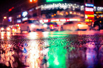 Wall Mural - Rainy night in the big city, dense traffic at a busy intersection in the light of shop windows. View from the level of asphalt