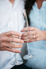 Two hands holding glasses of champagne toasting with engagement ring