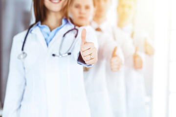 Wall Mural - Group of modern doctors standing as a team with thumbs up in sunny hospital. Medical help, insurance in health care, best desease treatment and medicine concept