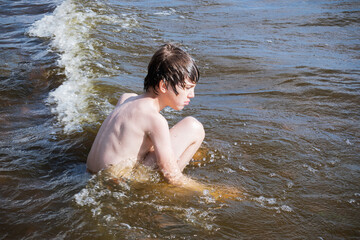 Pensive boy sitting in the surf among the waves.