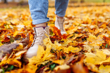 Legs of unrecognosable woman wearing brown boots and jeans in autumn yellow foliage walking in park or forest