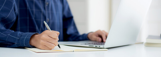 Closeup hand of business man writing on note while using laptop computer on desk at home, male planning on note for business success, author and blog, businessman working on table, employee and job.