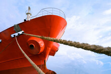 Low Angle View Of Cargo Ship Docked At Port With Mooring Rope Against White Clouds On Blue Sky Background