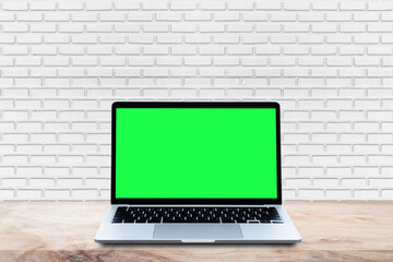 Wall Mural - Mockup Laptop computer blank green screen on wood table with white brick wall background.