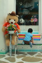Little Boy Sit On The Rainbow Bench By The Giant Teddy Doll.