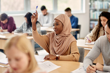 Muslim university student raising her hand to answer a question attending a class in the classroom.