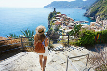 Tourism In Italy. Young Female Backpacker Going Downstairs In The Cinque Terre National Park. Beautiful Girl Walks The Azure Trail And Looking At Vernazza Town, Italy.