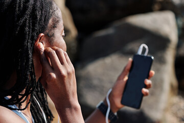 Wall Mural - Young woman putting in earbuds to make video all via smartphone