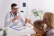 © LIGHTFIELD STUDIOS - Smiling doctor holding jar with pills near mother and kid