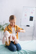 © LIGHTFIELD STUDIOS - Kid smiling while playing with soft toy and thermometer in clinic