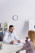 © LIGHTFIELD STUDIOS - doctor in white coat talking to blonde woman near clipboard with prescription