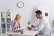 © LIGHTFIELD STUDIOS - doctor writing on clipboard while looking at woman touching sore throat during consultation