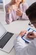 © LIGHTFIELD STUDIOS - cropped view of physician writing diagnosis near patient and laptop in consulting room