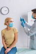 © LIGHTFIELD STUDIOS - woman in protective mask looking at doctor filling syringe with vaccine