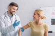 © LIGHTFIELD STUDIOS - positive doctor in latex gloves vaccinating happy woman in clinic