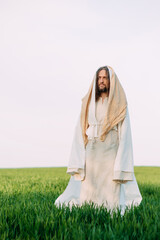 Wall Mural - Jesus Christ standing in meadow in white robe against sky background.
