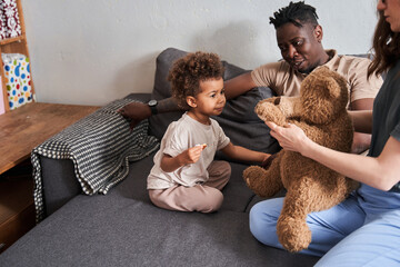 Wall Mural - Curly girl looking at her lovely teddy bear while her mother holding him