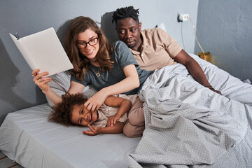 Wall Mural - Girl is smiling while her mother reading book with interest for her