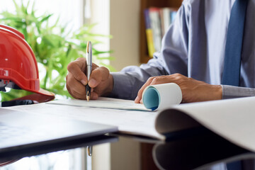 Wall Mural - Architect man or male engineer hand writing and sign cheque book, work on laptop computer with blueprint on the desk at office. 