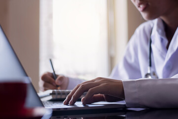 Doctor work on laptop computer and writing on notepad 