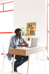 Wall Mural - African american male painter at work using laptop in art studio