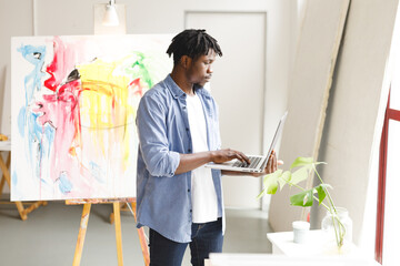 Wall Mural - African american male painter at work using laptop in art studio