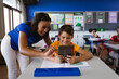 African american female teacher teaching a boy to use digital tablet in class at elementary school