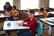 © WavebreakMediaMicro - Portrait of caucasian boy with laptop smiling while sitting on his desk at elementary school