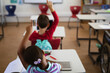 © WavebreakMediaMicro - Rear view of african american girl raising her hand while sitting on her desk at elementary school