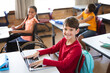 © WavebreakMediaMicro - Portrait of caucasian boy with laptop smiling while sitting on his desk at elementary school