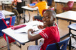 © WavebreakMediaMicro - Portrait of african american boy smiling while sitting on his desk in the class at elementary school