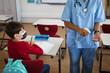 © WavebreakMediaMicro - Mid section of female health worker showing students to use hands sanitizer at elementary school