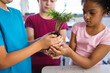 © WavebreakMediaMicro - Mid section of diverse students holding a plant seedling together in the class at elementary school