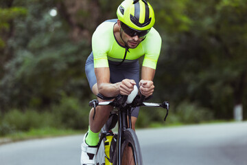 Wall Mural - Young male triathlete riding a bicycle on the open road. Professional sportsman is engaged in triathlon on bright summer day