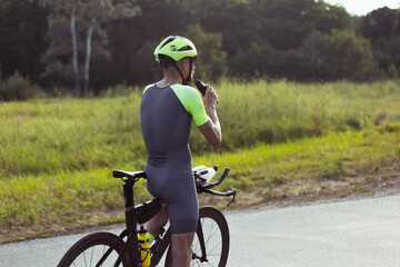 Wall Mural - Young male triathlete riding a bicycle on the open road. Professional sportsman is engaged in triathlon on bright summer day