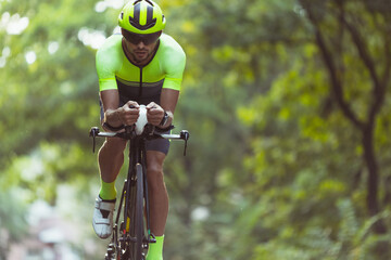 Wall Mural - Young male triathlete riding a bicycle on the open road. Professional sportsman is engaged in triathlon on bright summer day