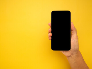 Wall Mural - hand holding of a smartphone with a yellow background. close-up photo. space for text. technology an