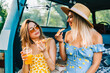 Two attractive cheerful women drinking lemonade near van and eating pizza, enjoying summer vibes in road trip