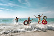 © cppzone - Happy cheerful friends resting on a beautiful beach at sunny day and running into the sea with inflatable rings. Tropical vacations concept